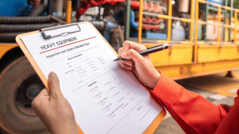 maintenance worker going over heavy equipment checklist on a clipboard with a pen
